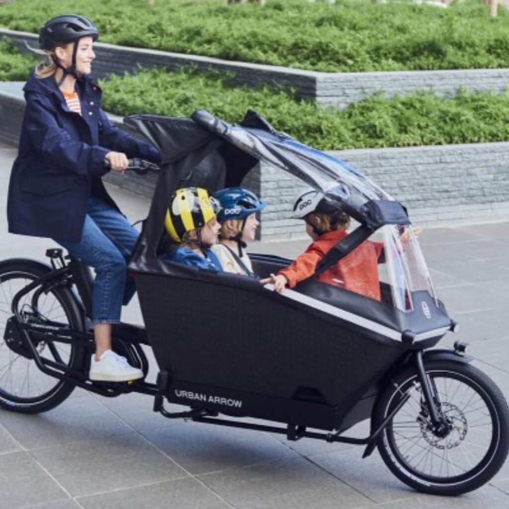 Urban Arrow Family E-Cargo Bike with adult rider and 3 children riding in the basket