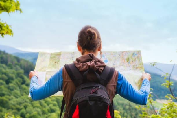 Hiking woman traveler with backpack checks map to find directions in wilderness area,