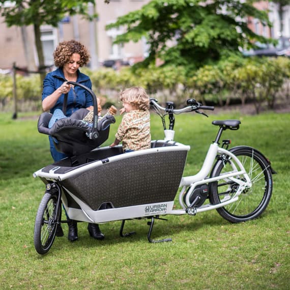 Urban Arrow Family eBike, adult standing with children, one in the bike basket, and one in a child seat